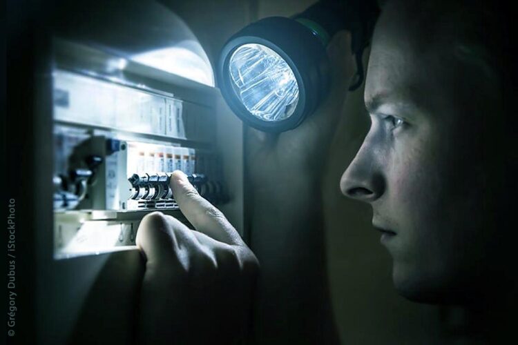 Mann bei Dunkelheit beleuchtet mit Taschenlampe einenSicherungskasten